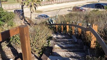 Un escalier en bois mène à une plage d’où l’on a une vue dégagée sur l’océan, avec une rangée de bâtiments blancs en arrière-plan.