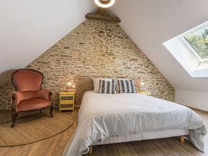 Una camera da letto con parete in pietra, un letto con lenzuola a righe, una sedia di legno e un lucernario.