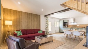 A modern living space with a red sofa, a leather chair, a wooden coffee table, and a kitchen area with a dining table and chairs. - Peaceful country cottage - 6 guests (Nort-sur-Erdre)