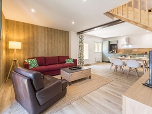 A modern living space with a red sofa, a leather chair, a wooden coffee table, and a kitchen area with a dining table and chairs. - Peaceful country cottage - 6 guests (Nort-sur-Erdre)