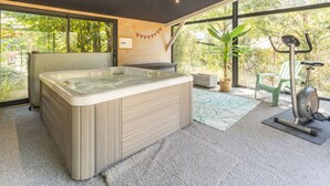 A modern bathroom with a large bathtub, a green exercise bike, and a view of greenery outside. - Peaceful country cottage - 6 guests (Nort-sur-Erdre)