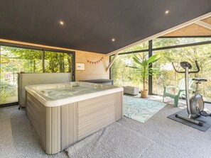 A modern bathroom with a large bathtub, a green exercise bike, and a view of greenery outside. - Peaceful country cottage - 6 guests (Nort-sur-Erdre)