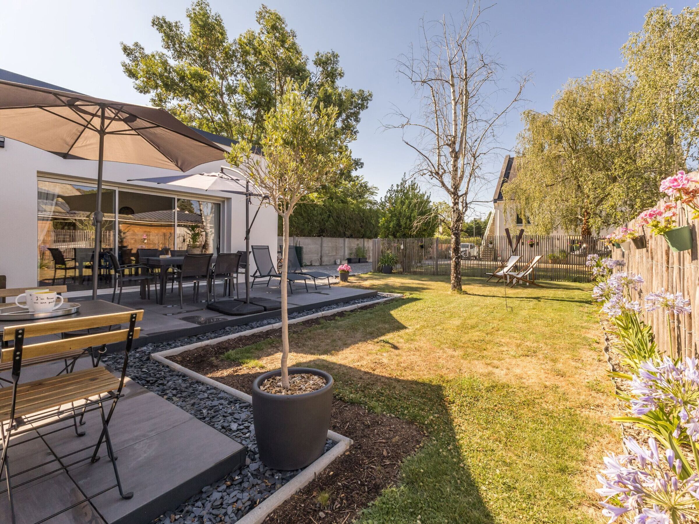 A backyard with a patio, outdoor seating, a tree, and a wooden fence.
