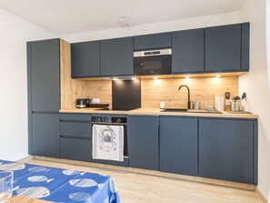 Eine kleine Küche mit dunklen Schränken, einer Holzarbeitsplatte, einem eingebauten Backofen und einem Spülbecken.