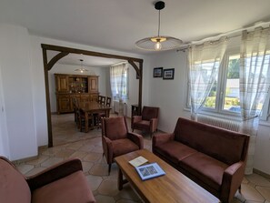 Un vaste espace de vie comprenant une table à manger en bois, des sièges confortables et une vue dégagée grâce à de grandes fenêtres.
