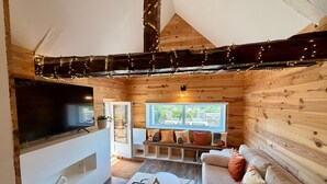 Ein gemütliches Blockhaus-Interieur mit Fernseher, Sitzecke, Holzwänden und einem Fenster mit Aussicht.