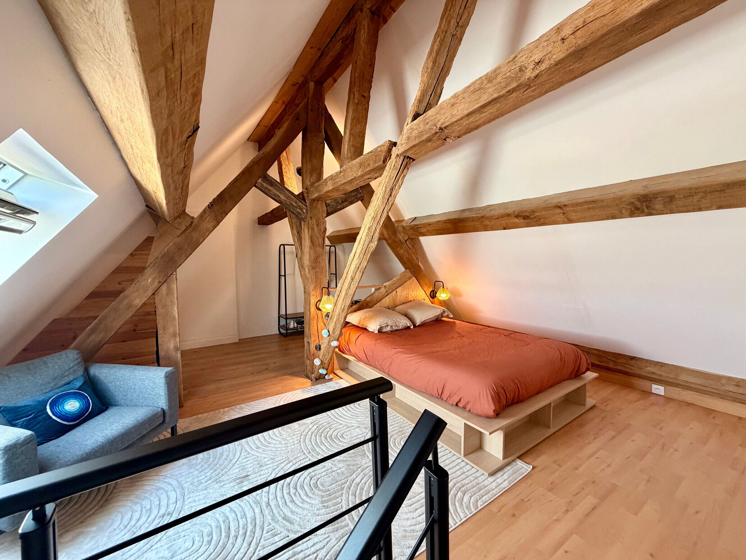 Ein Schlafzimmer im Loft-Stil mit freiliegenden Holzbalken, einem Bett, einem Schreibtisch und einem Sessel.