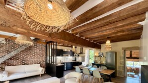 Ein großzügiger Wohnbereich mit Sofa, Sessel und Couchtisch. Im Hintergrund ist eine Küche mit modernen Geräten zu sehen.