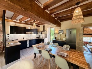 A modern kitchen with dark cabinets, a central island, and a dining area with a wooden table and chairs.