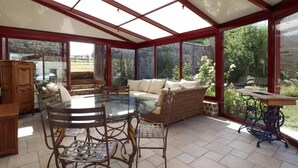 Ein Wintergarten mit einem Glastisch und Stühlen, einem Sofa und einem Holzschrank.