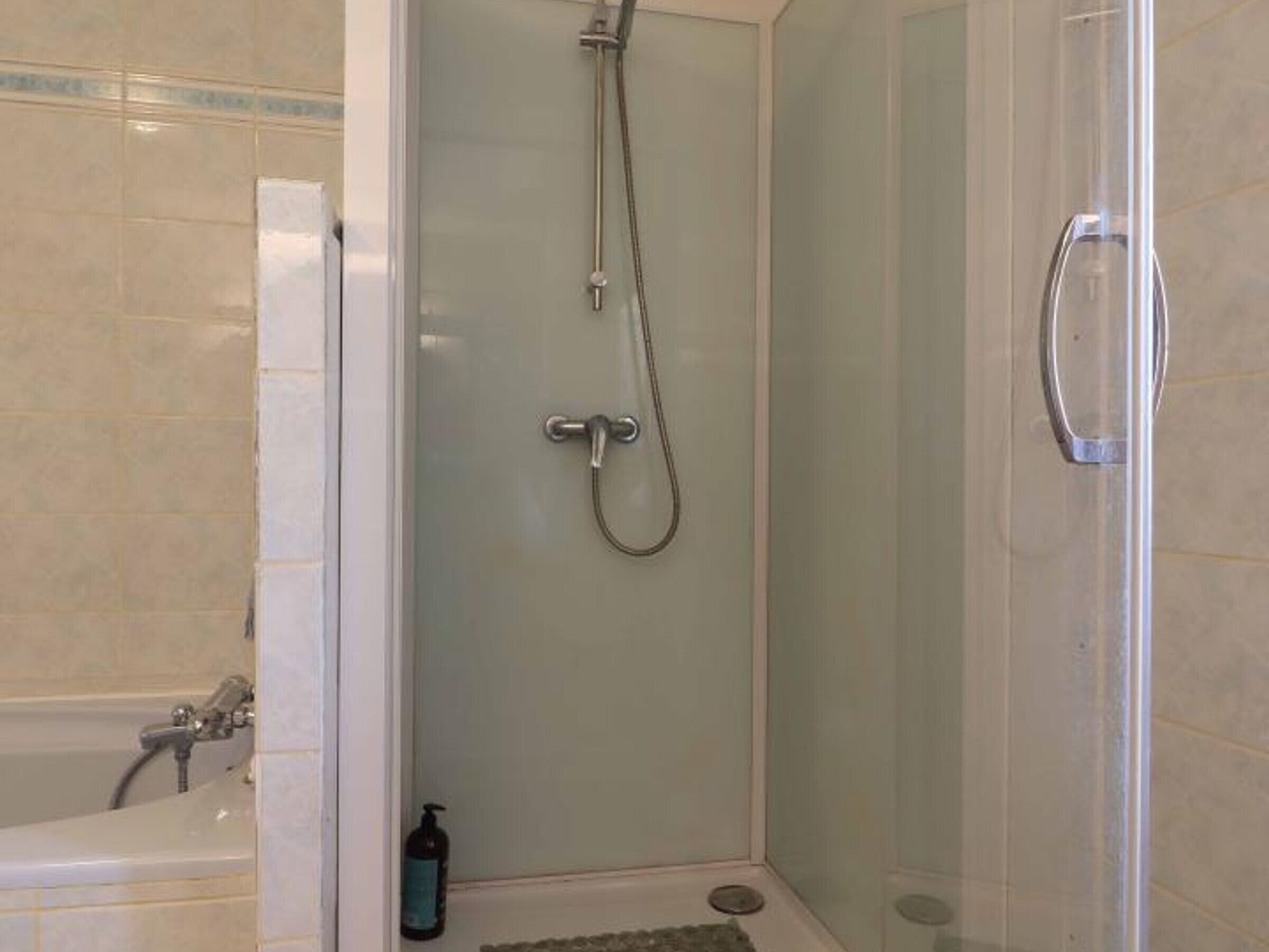 A glass-enclosed shower with a handheld showerhead and a wall-mounted faucet.