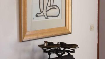 Una obra de arte enmarcada en una pared, un estante metálico de estilo antiguo con un objeto pequeño encima, e interruptor de luz en la pared.