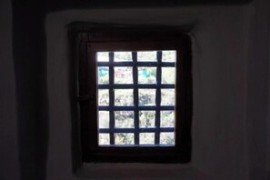 Ein kleines Fenster mit Gittermuster, durch das Licht in einen schwach beleuchteten Raum fällt.