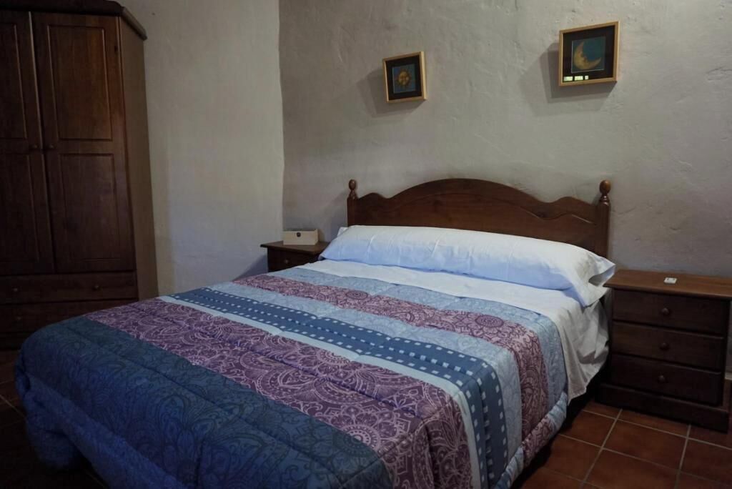 Un dormitorio con cama de madera, una mesita de noche, un armario y dos cuadros colgados en la pared.