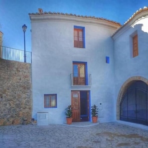 A two-story building with a balcony, a stone wall, and a metal gate. - Cau de lárt (Llucena)