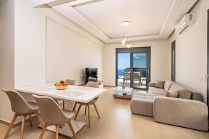 Ein modernes Wohnzimmer mit Essbereich, einer Couch und Meerblick durch eine Glasdoor.