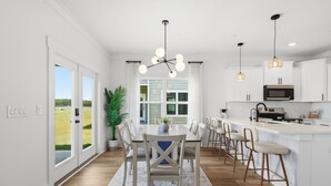 A modern kitchen with white cabinetry, a central island, and a dining area with a table and chairs. - Sea La Vie / Sleeps 8 / Game Room / Just 5 min away from the beach (Panama City Beach)