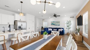 A modern kitchen with white cabinets, a dining area with a wooden table, and a living room with a blue sofa. - Sea La Vie / Sleeps 8 / Game Room / Just 5 min away from the beach (Panama City Beach)