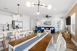 Eine moderne Küche mit weißen Schränken, ein Essbereich mit einem Holztisch und ein Wohnzimmer mit einem blauen Sofa.