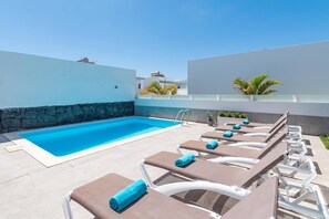 Zona de piscina amb una piscina rectangular, gandules i plantes en testos.
