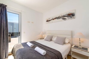 Ein Hotelzimmer mit einem Bett, zwei Nachttischen, einem Gemälde und Blick durch eine Glastür.