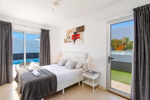 Ein modernes Schlafzimmer mit Bett, Nachttisch und Blick auf Pool und Grünflächen.