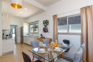 Eine moderne Küche mit Fenster, ein Essbereich mit Glastisch und ein Wohnbereich mit Sofa.