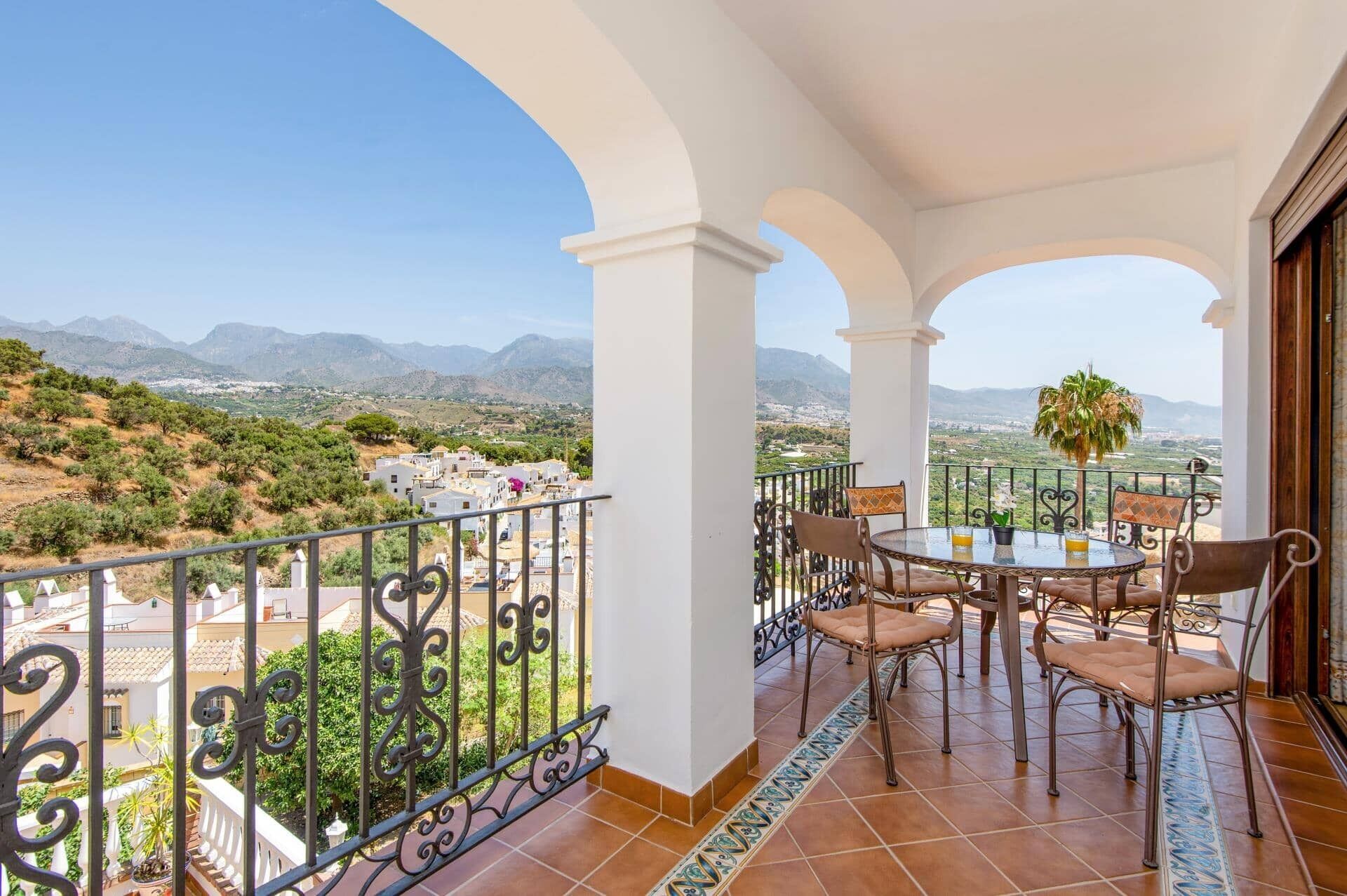 Un balcon avec une table et des chaises, une vue sur la campagne et une chaîne de montagnes à l’horizon.