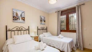 A hotel room with two beds, a nightstand, a window with curtains, and two paintings on the wall. - Villa Lara Pinta by Villa Plus (Nerja)