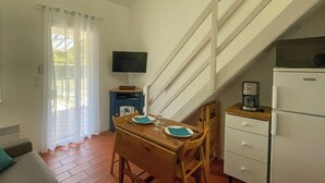 Un espacio habitable compacto con una mesa de comedor lista para dos personas, un sofá, una zona de cocina con refrigerador y un televisor en la pared.