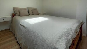 Un dormitorio con cama, mesita de noche y suelo de madera.
