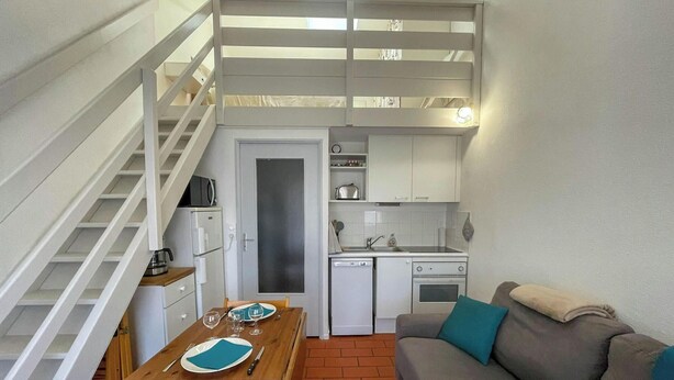 Un espacio habitable compacto con kitchenette, comedor y una escalera que lleva a una planta superior.