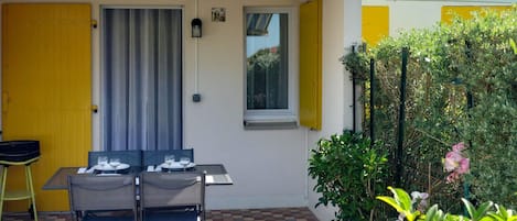 Une terrasse avec une table et des chaises, une porte jaune et une fenêtre avec des volets jaunes.