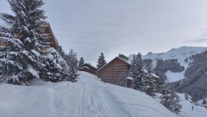 A snow-covered mountain path leading to wooden cabins with a forest backdrop and distant mountains. - Apartment with mountain view - 8 guests (Méribel)