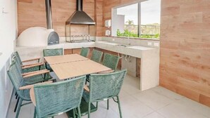 A modern kitchen with a built-in grill, a dining area with wicker chairs, and a large window providing a view. - Fully furnished apartment with TV and free internet. (São Paulo)