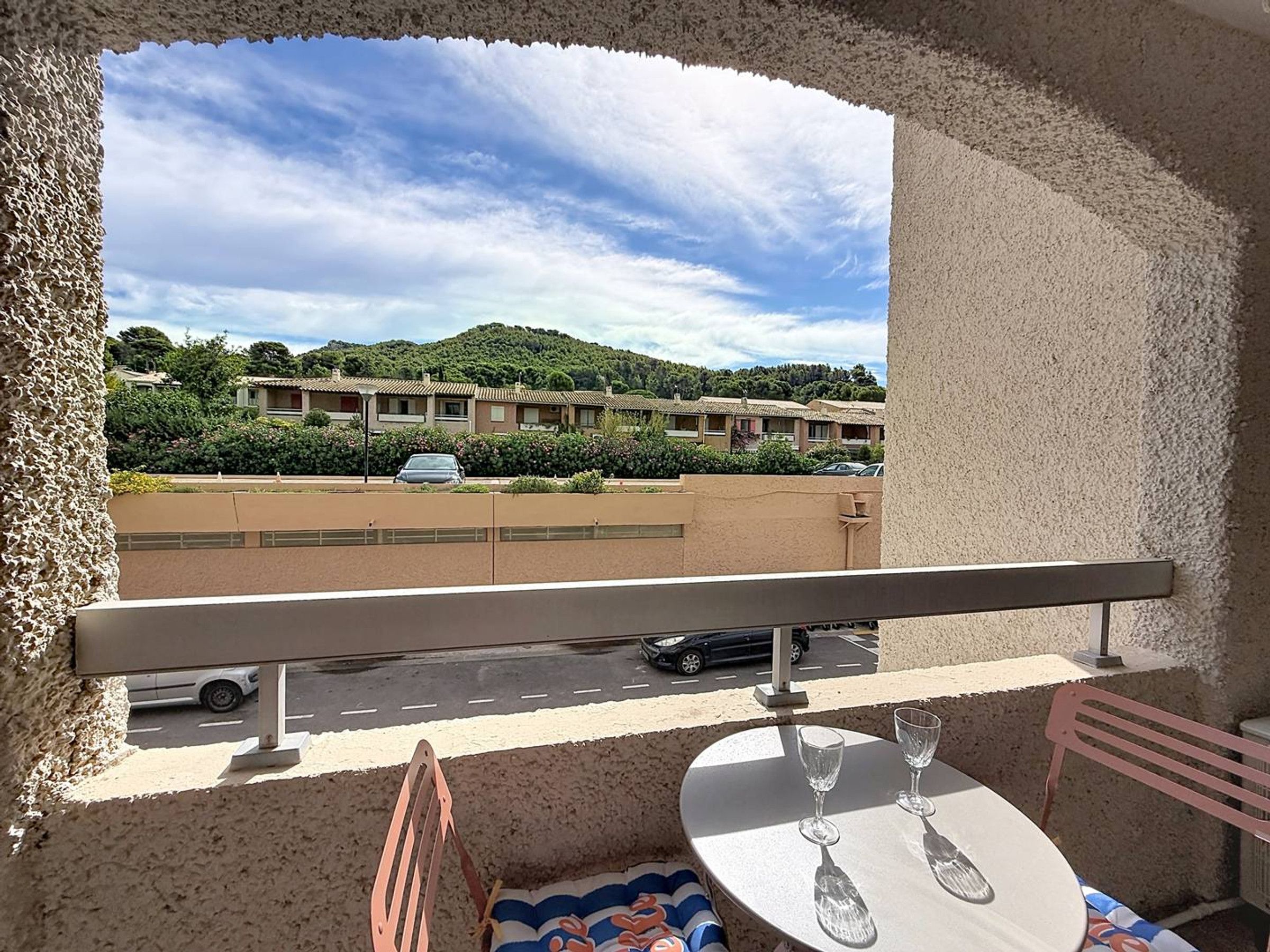 Ein Balkon mit Tisch und Stühlen, der auf einen Parkplatz und ein Gebäude mit vielen Fenstern blickt.