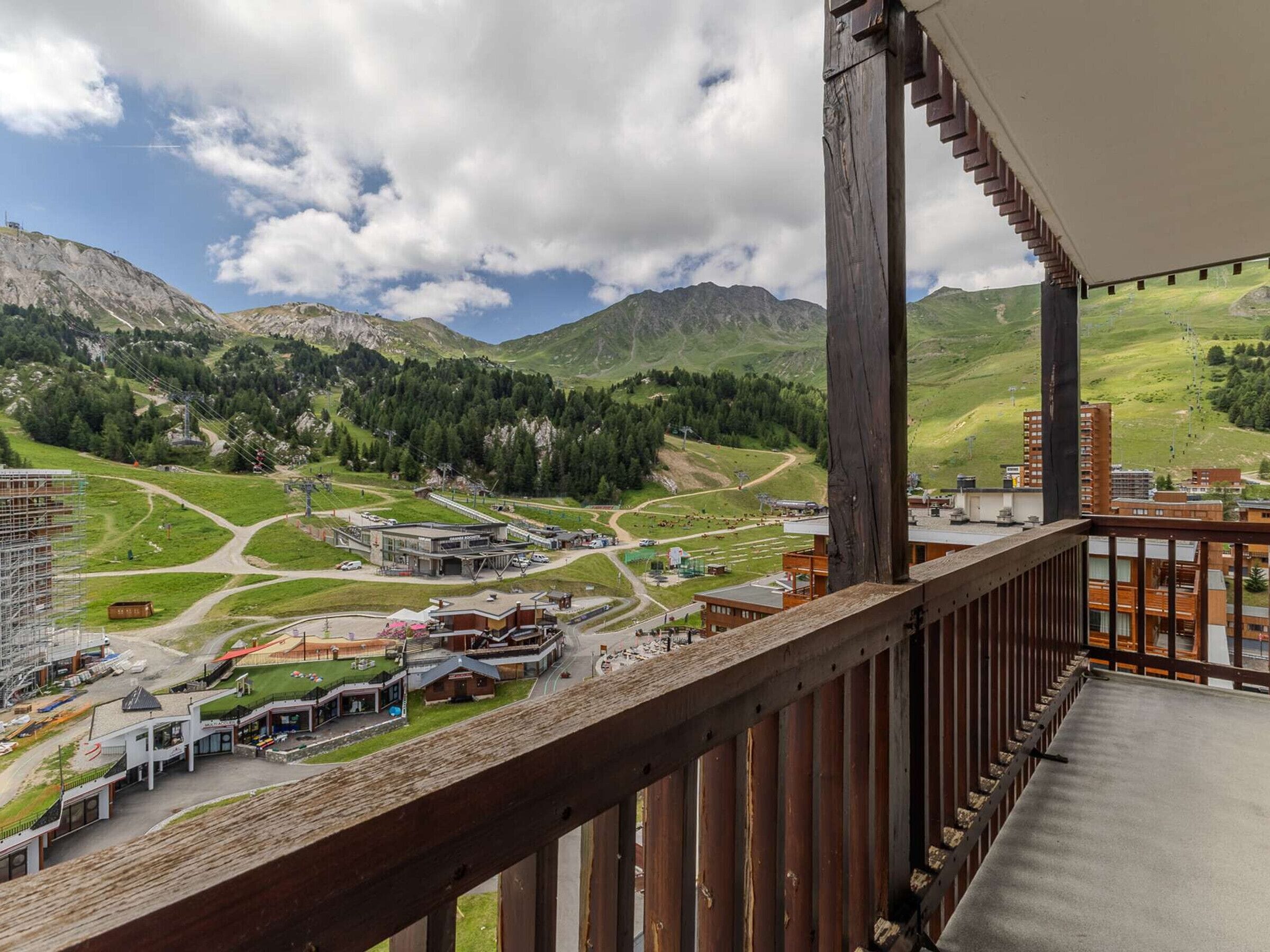 A balcony with a view of a mountainous landscape, a ski resort, and a building with a modern design.