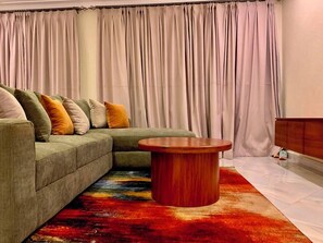 A living room with a sectional sofa, a round wooden coffee table, and a colorful rug. - Perfect 2-bedroom apartment in Entebbe for a relaxing stay (Entebbe)