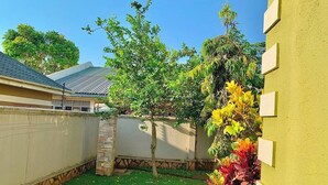 Un giardino privato con prato verde, un albero e un muro giallo.
