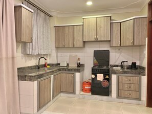 A compact kitchen with wooden cabinets, a gas stove, a coffee maker, and a toaster. - Perfect 2-bedroom apartment in Entebbe for a relaxing stay (Entebbe)