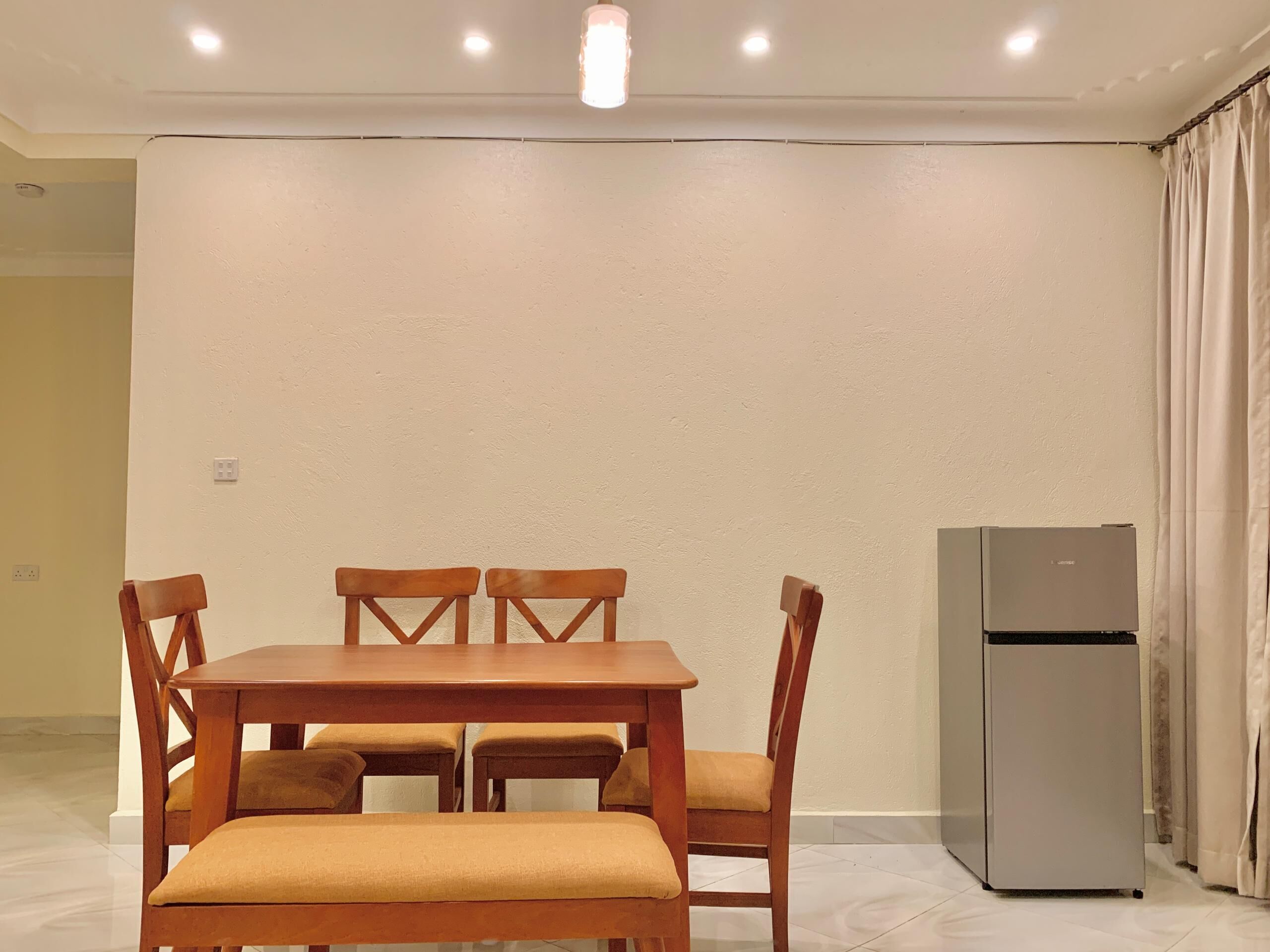 A dining area with a wooden table and chairs, a refrigerator, and a plain wall.