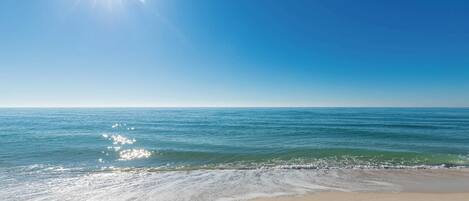 Ein Strand mit blauem Himmel und Sonnenlicht, das sich im Wasser spiegelt.
