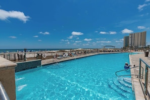 Ein Pool mit Blick auf Strand und Meer, umgeben von Liegestühlen und Sonnenschirmen.