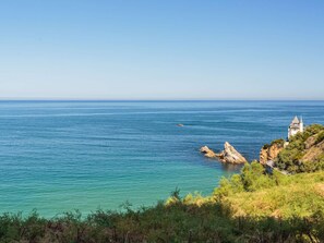 Eine Küstenlandschaft mit klarem, blauem Meer, Felsformationen und einem kleinen Gebäude auf einer Klippe.