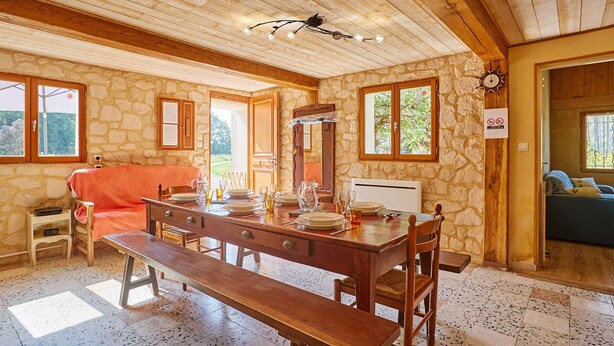 Un comedor rústico con una mesa de madera dispuesta para cuatro personas, paredes de piedra y un banco.