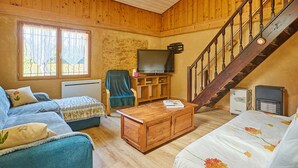 Una sala de estar acogedora con detalles de madera, un sofá, una mesa de centro, un televisor y una escalera.