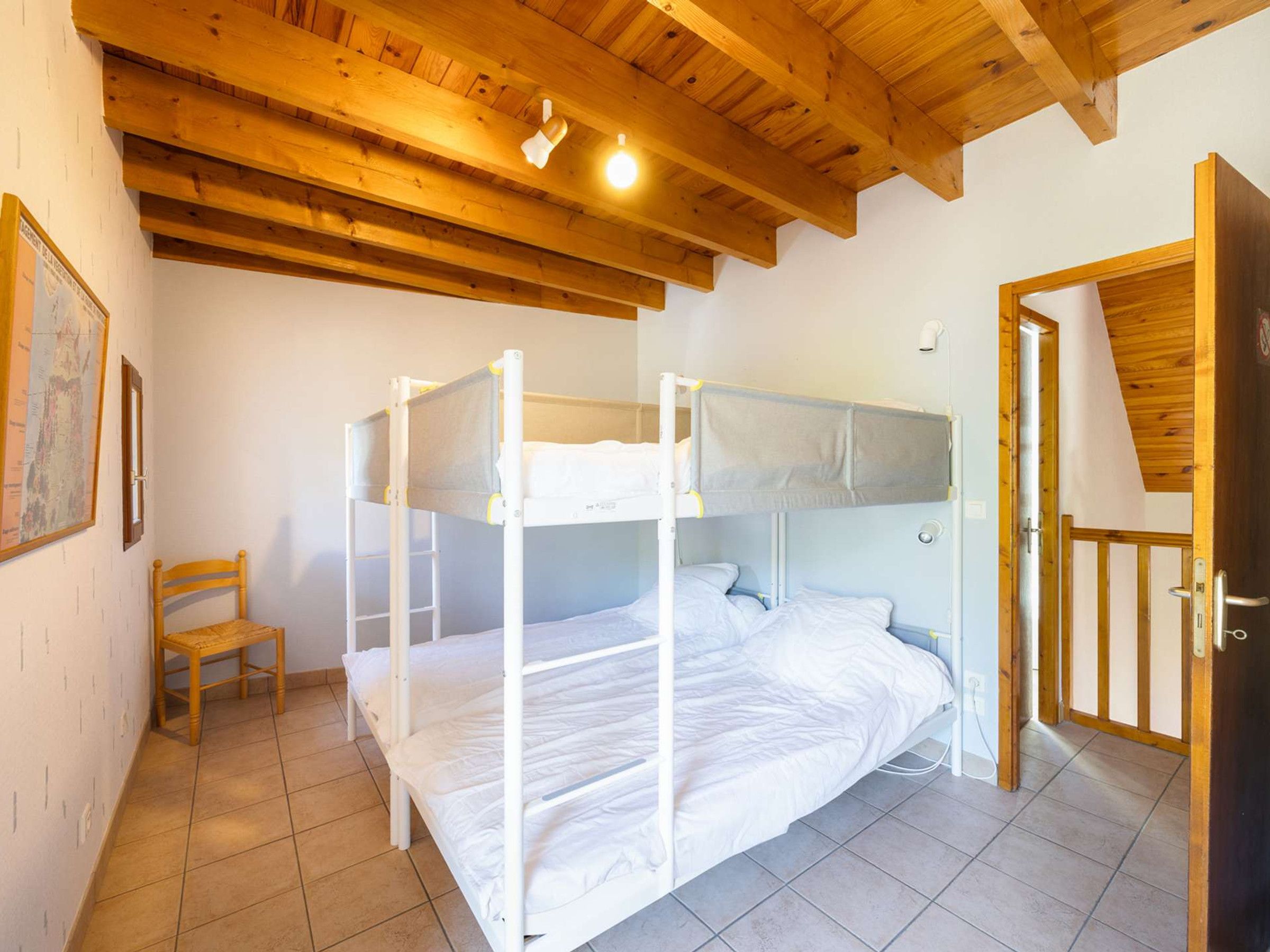 Een kamer met een stapelbed, een houten stoel en een deur.