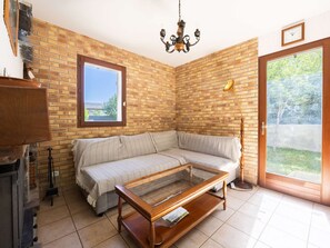 A room with a brick wall, a wooden sofa, a glass coffee table, a chandelier, and a door leading outside. - Large house, pets allowed - 10 guests (Vielle-Aure)
