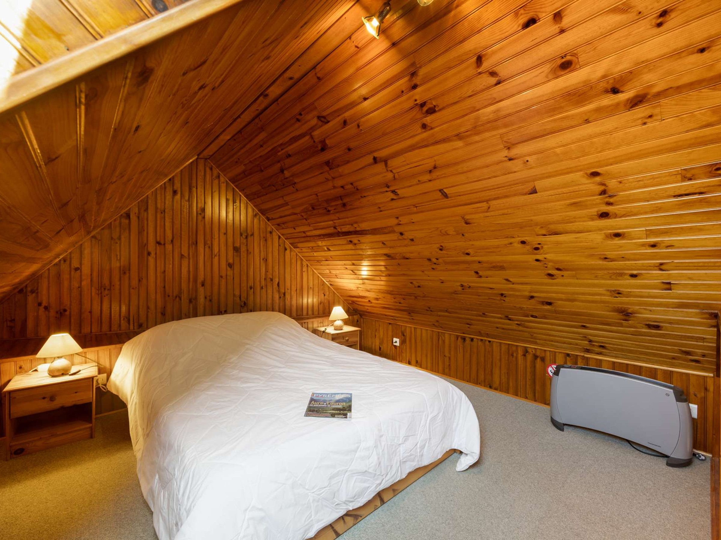 Een slaapkamer met een houten schuine plafond, een enkel bed, een nachtkastje met een lamp en een radiator.