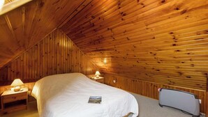Une chambre avec un plafond en pente en bois, un lit, une table de chevet avec une lampe et un radiateur.